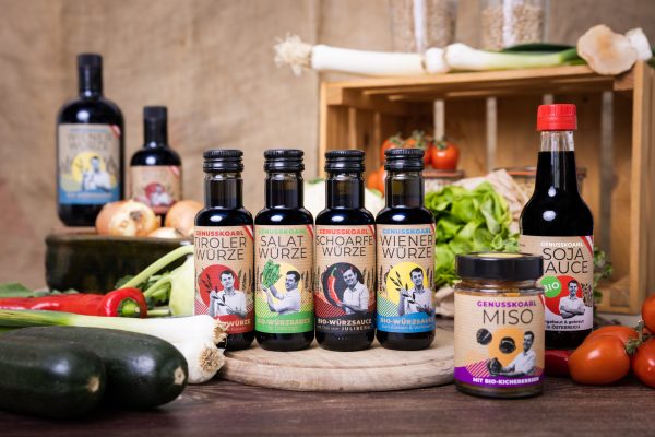 Genusskoarl Produktpalette: Bio-Würzsaucen und Misos auf Holzplatte, bunt etikettiert