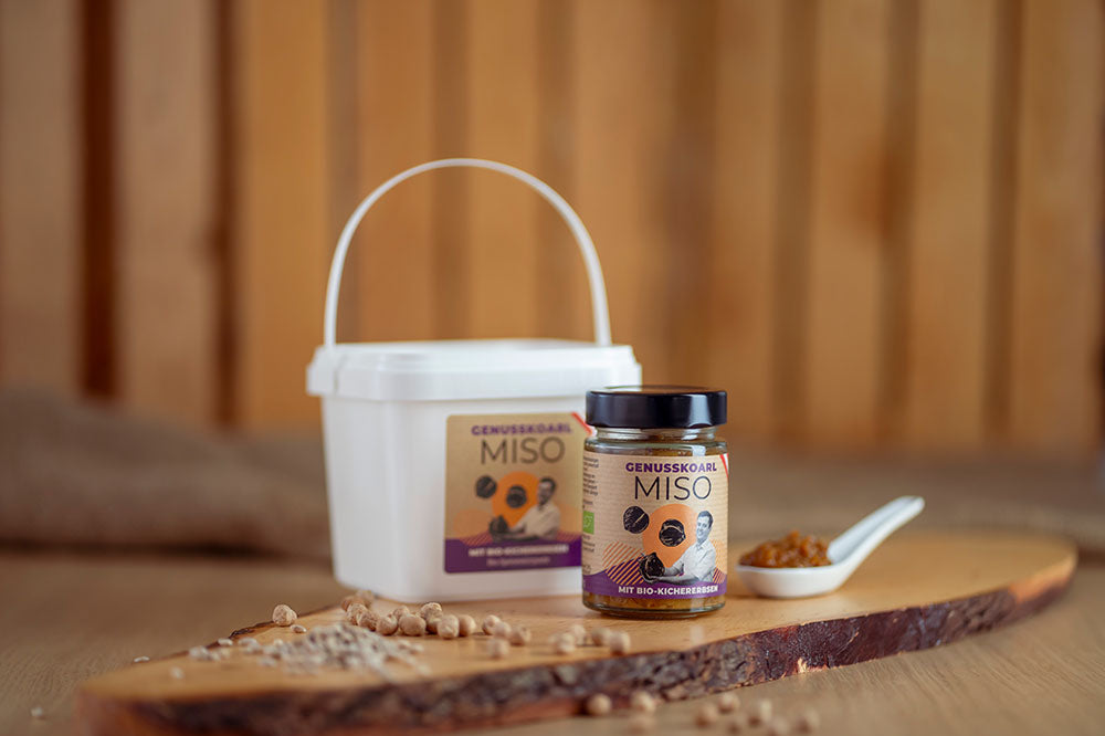 Würzpaste Genusskoarl Bio-Kichererbsen Miso in einem 190 g Glas und einem 1 kg Eimer auf Holzbrett