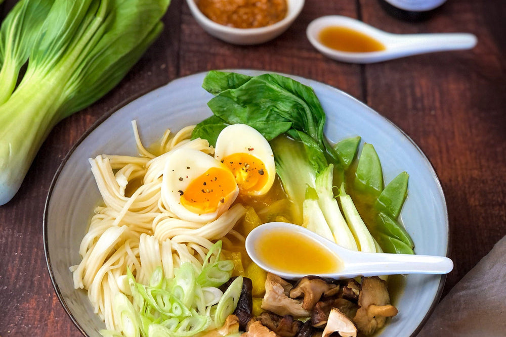 Quadratisches Flatlay: Schüssel aromatische Ramen-Suppe mit Reisnudeln, Frühlingszwiebeln, Eihälfte und misoroter Brühe. Modernes, einladendes Food-Styling.