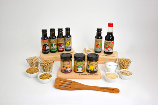Genusskoarl Sortiment: mehrere Glasflaschen mit Bio-Sojasauce, Bio-Würzsauce und Miso-Gläsern. 